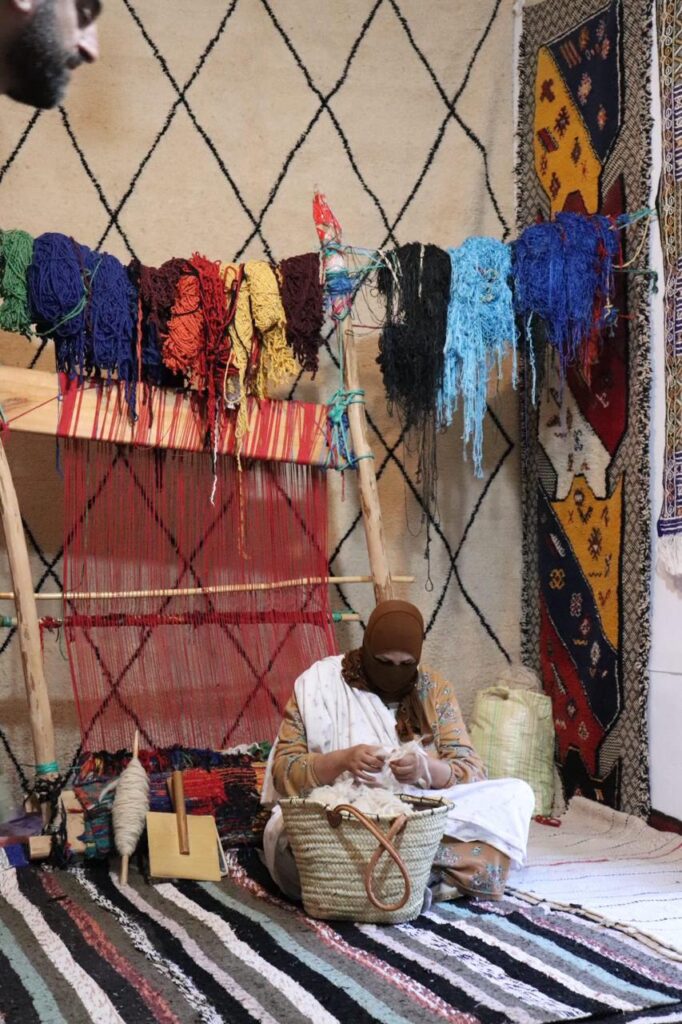 Handmade Moroccan Rugs - Berber artisan woman weaving traditional handmade Moroccan rug on wooden vertical loom in Atlas Mountains village workshop